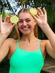 Cheeky image of Soraya holding limes wearing JAYD Swimwear tie back athletic full coverage one piece: Riva in Meadow