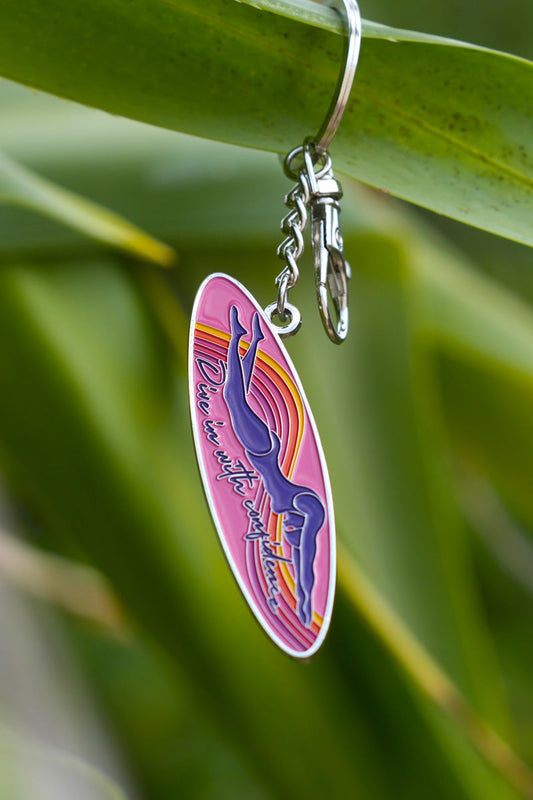 JAYD Swimwear keyring featuring a woman diving into the water with the phrase 'dive in with confidence' on a colourful ink surfboard shape.