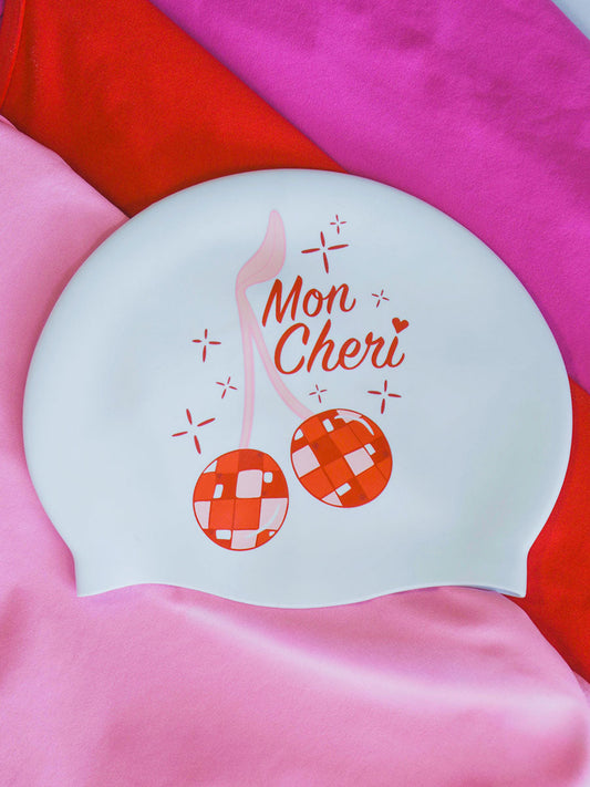 White JAYD swim cap on a pink background with cherry disco balls and text 'Mon Cheri'.