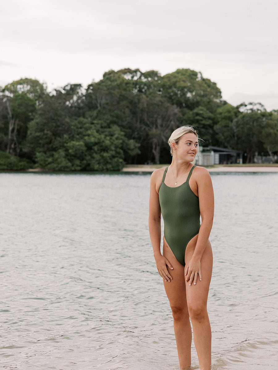 Woman in a green swimsuit standing by a lake with trees in the background