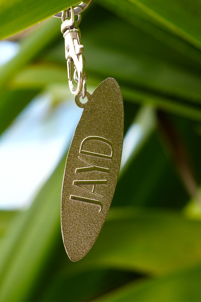Gold keychain with 'JAYD' engraving against a green leafy background