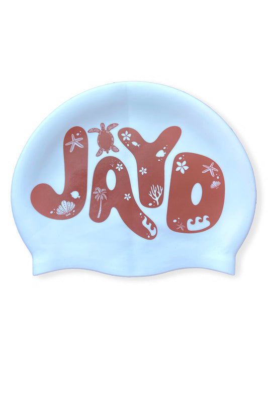 White JAYD Swimwear swim cap in brown bubble letters with tropical island palm trees, turtle and shell icons.