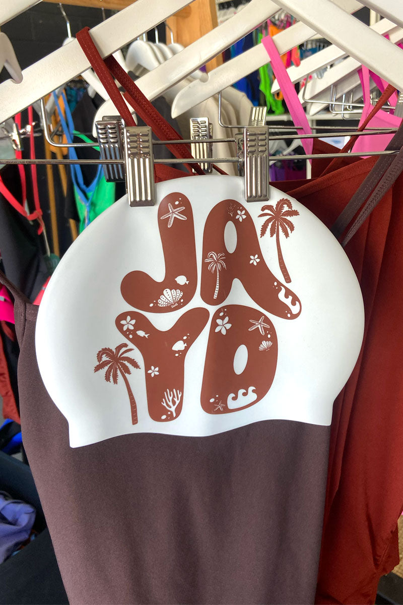 Brown and white swim cap with 'JAYD' design hanging on a rack.